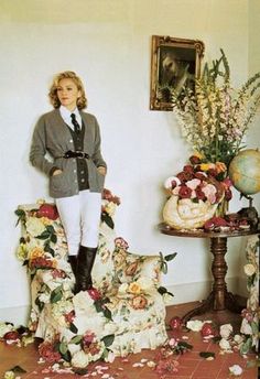 a woman standing next to a chair with flowers all over it and a painting on the wall