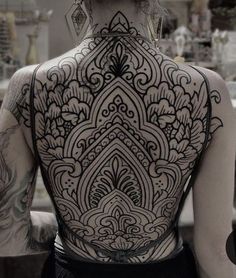 the back of a woman's body covered in black ink with intricate designs on it