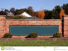 a brick wall with a green sign in front of it and trees around the perimeter