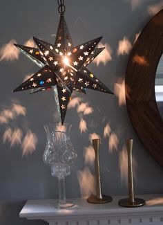 a lighted star hanging from the ceiling next to a wine glass and candle holder on a mantle