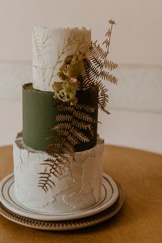 a three tiered cake with white frosting and greenery on top, sitting on a plate