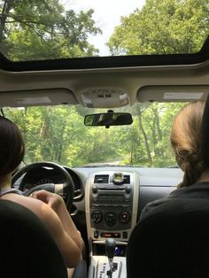 two people sitting in the driver's seat of a car with trees in the background