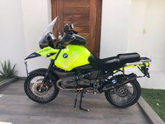 a yellow and black motorcycle parked in front of a door with grass on the side