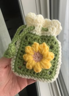 a hand holding a crocheted purse with a flower on the front and side