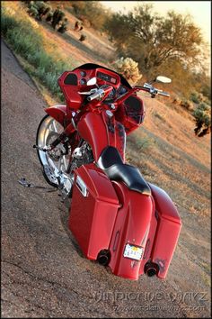 a red motorcycle parked on the side of a road next to grass and trees in the background