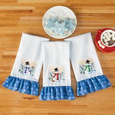 two kitchen towels with snowmen on them next to a bowl of marshmallows