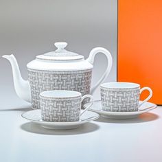 the tea set is white and has gray designs on it, along with an orange box