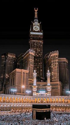 a large clock tower in the middle of a city with tall buildings behind it at night