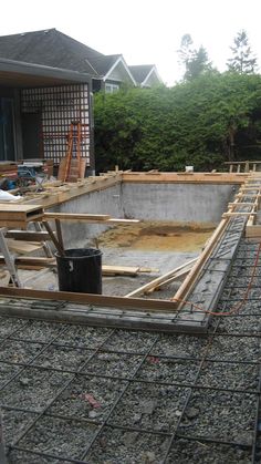 an unfinished pool is being built in the backyard with wood framing around it and construction tools on the ground