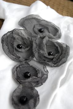 three black flowers are sitting on top of a white shirt and some brown material is laying on the floor