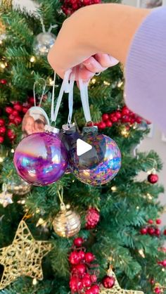 someone holding ornaments in front of a christmas tree