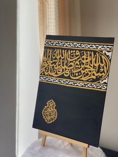 an open book with arabic writing on it sitting on a wooden easel in front of a window