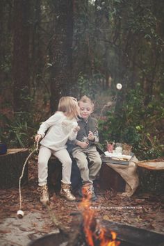 two children sitting at a campfire in the woods