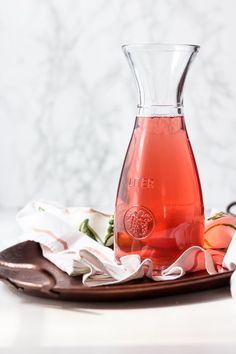 a glass vase filled with liquid sitting on top of a wooden plate next to flowers