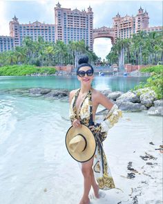 a woman standing on top of a beach next to the ocean wearing a hat and sunglasses