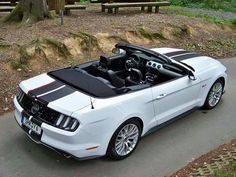 a white ford mustang convertible parked in front of a park bench