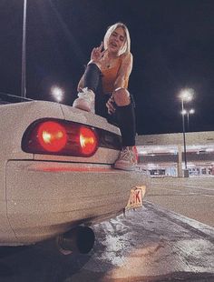 a woman sitting on the hood of a white sports car in front of an empty parking lot