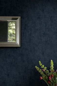 a vase filled with flowers sitting next to a mirror on a blue wall behind it