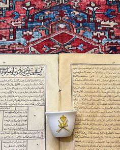 an open book with arabic writing on it and a cup in front of the page