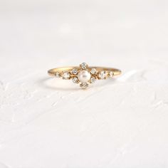 a gold ring with three diamonds and a pearl on the front, sitting on a white surface