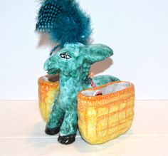 an elephant figurine sitting next to a basket with feathers on it's head