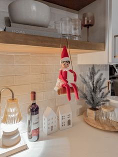 an elf is hanging from the kitchen shelf with wine bottles and other decorations on the counter