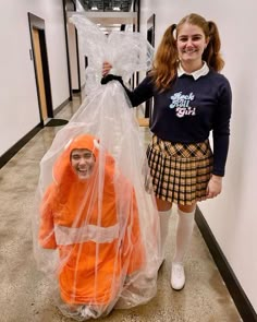 a girl in an orange costume is standing next to a plastic bag and smiling at the camera