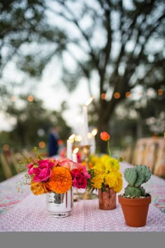 colorful flowers are sitting on a table with candles and potted cacti in the background