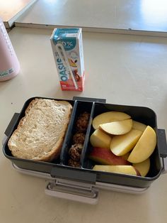 a lunch box with two compartments filled with food and an apple slice next to a carton of yogurt