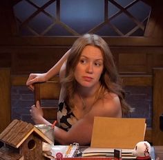 a woman sitting at a table in front of a birdhouse and other items on the table