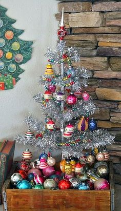 a small christmas tree with ornaments in a wooden crate next to a stone wall and fireplace