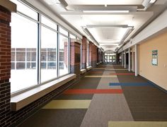 an empty hallway with lots of windows and colorful carpeted flooring on both sides