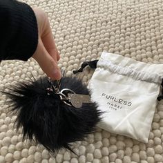 a hand holding a fur ball keychain on top of a white bag next to a purse