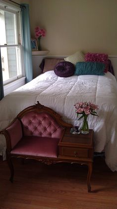 a bedroom with a bed, chair and table in it's corner next to a window