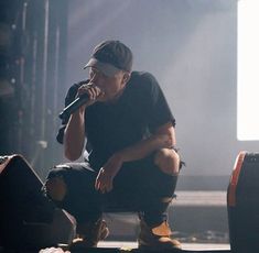 a man sitting on top of a stage while holding a microphone to his mouth,