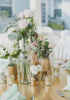 a table topped with vases filled with flowers and greenery next to silverware