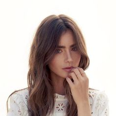 a woman with long brown hair wearing a white shirt and holding her hand to her face