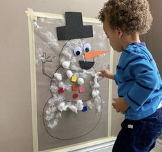 a young boy painting a snowman on a bulletin board with magnets attached to it