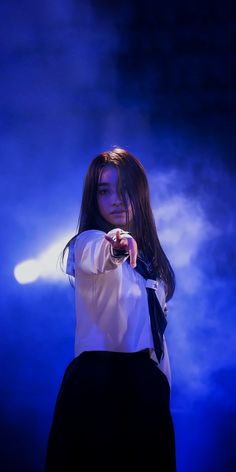 a woman in white shirt and black skirt standing on stage with blue light behind her