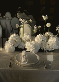 the table is set with white flowers and silverware