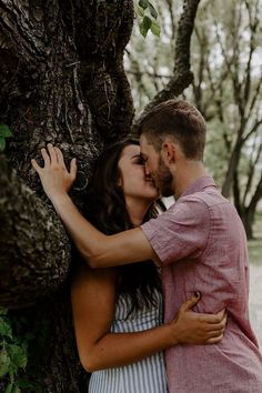 a man and woman kissing in front of a tree