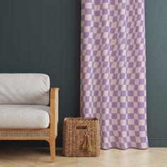 a chair sitting next to a window with a purple checkered curtain behind it and a basket on the floor