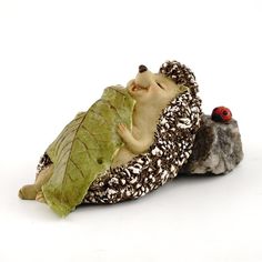 a ceramic figurine of a hedge holding a leaf and a bird perched on it's back