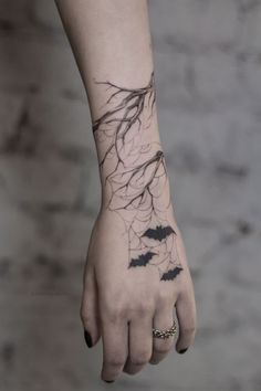 a woman's hand with black ink on it and bats flying through the branches