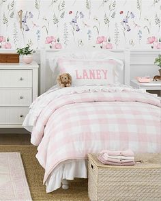 a pink and white bedroom with flowers on the wall, bed linens and pillows