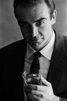 a man wearing a suit and tie holding a glass in his hand with the words booze like bond on it