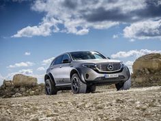 the mercedes benz suv is parked in front of some rocks and boulders, under a blue sky with white clouds