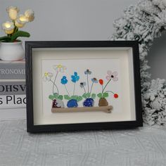 a picture frame with flowers in it on a table next to books and a potted plant