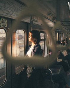 a woman sitting on a train looking out the window at other people in the background