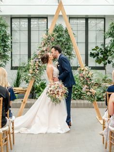 a bride and groom kissing in front of an arch decorated with greenery